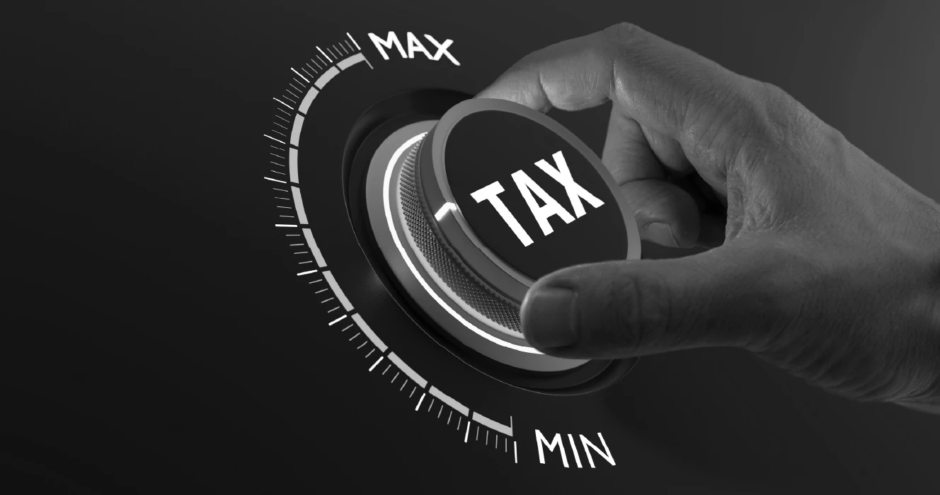 Black and white close up image of a hand turning up a dial labeled 'TAX'